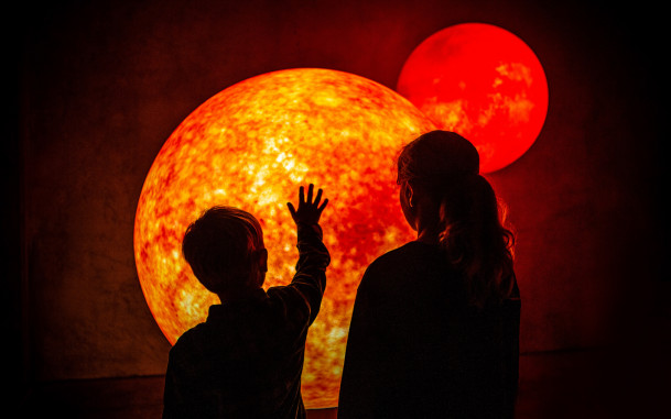 Two children standing in front of model of glowing planet