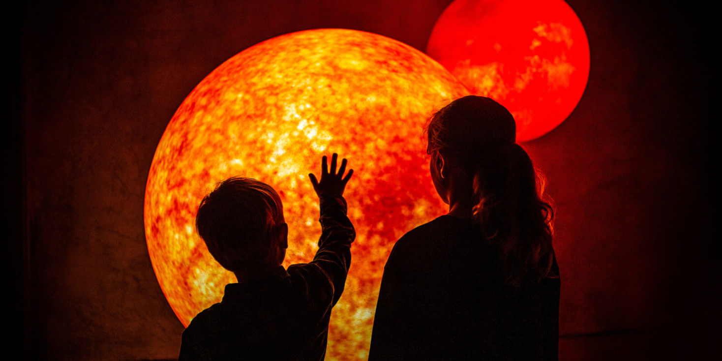 Two children standing in front of model of glowing planet