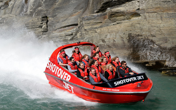 Jet boat speeds along river with rocky cliff in background